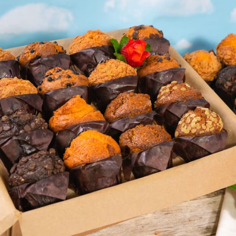 A box filled with assorted muffins, including chocolate chip, plain, and oat-topped, with a strawberry garnish.