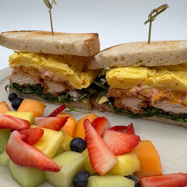 Chicken and egg sandwich with lettuce and sauce, served with a side of mixed fruit.
